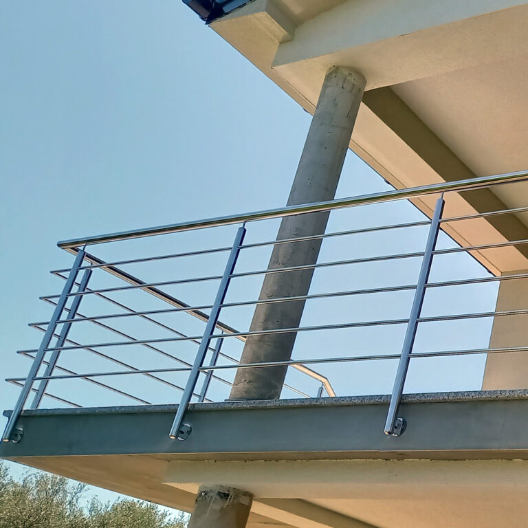 Moderni balkon s ogradama od inoxa i mesinga i betonskim stupom, gledan odozdo naspram vedrog plavog neba.