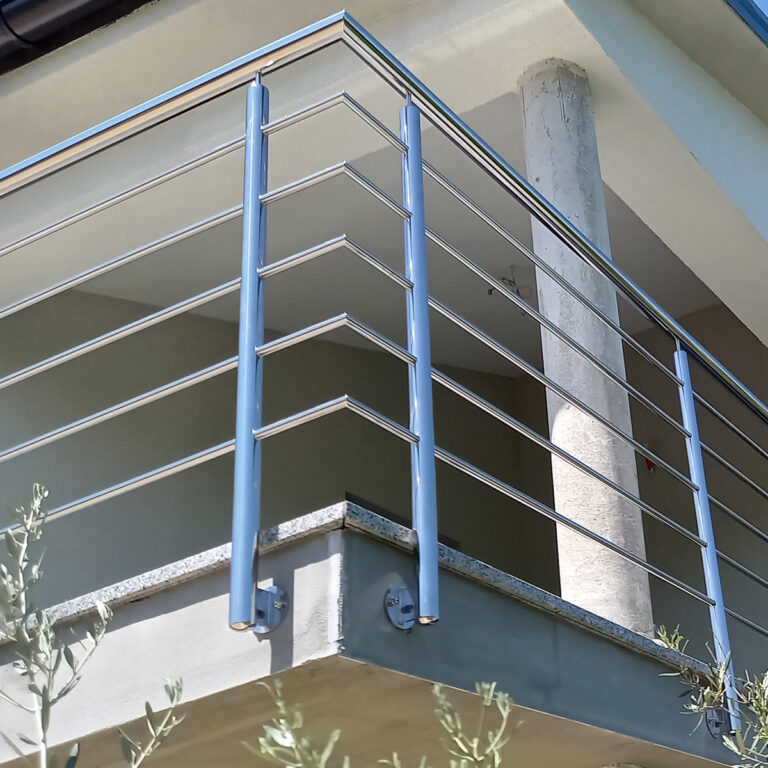 Moderni kutni balkon s elegantnom ogradom od nehrđajućeg čelika i mesinga, s horizontalnim šipkama na svijetloj zgradi. Betonski stup podupire krov iznad, dok živo zelenilo dodaje šarm u prvom planu.