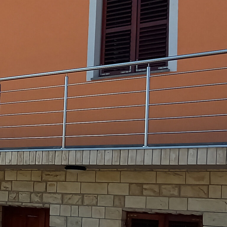 Pročelje zgrade s narančastim zidom, zatvorenim prozorom s tamnim kapcima, ograde od inoxa i mesinga i donji dio od svijetlih kamenih cigli.