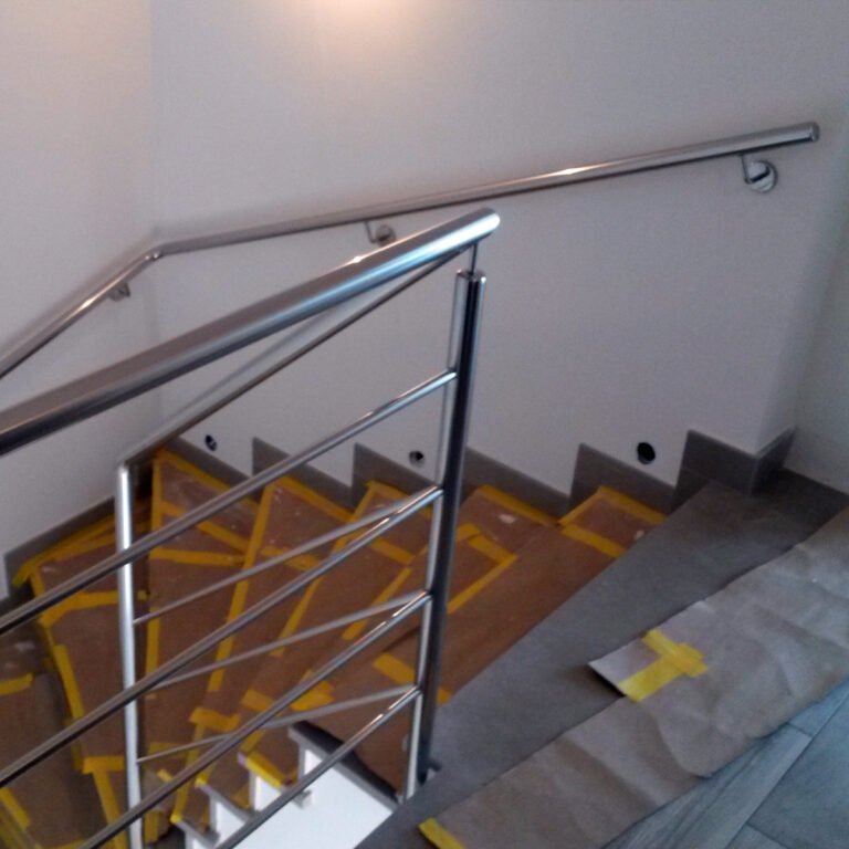 Stubište s Unutrašnjom ogradom od inoxa djelomično je prekriveno zaštitnim kartonom i žutom trakom. Zid je bijel, a iznad stepenica nalazi se rasvjetno tijelo.