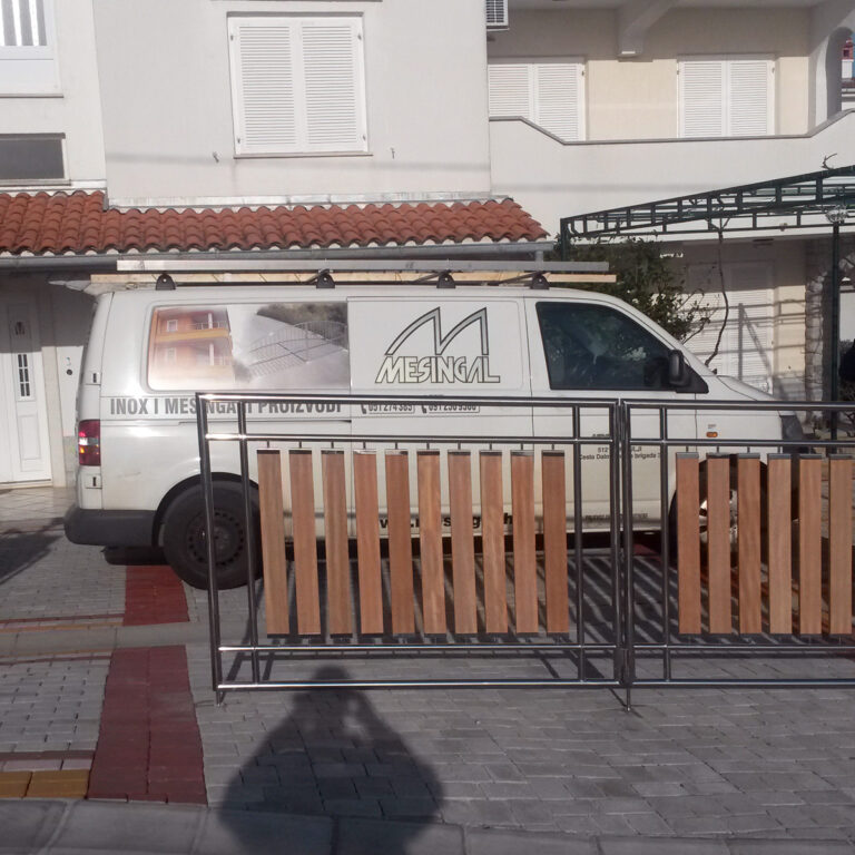 Bijeli kombi s logotipom MESINAL i kontaktnim podacima parkiran je ispred kuće s crvenim crijepnim krovom i bijelim kapcima. Na bočnoj strani kombija nalaze se slike metalnih radova, uključujući portuni od inoxa, zajedno s telefonskim brojem.