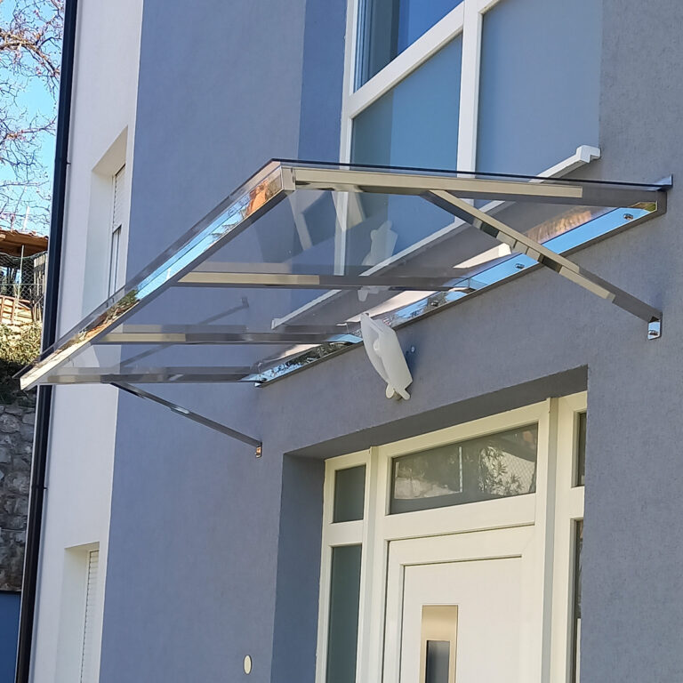 Moderna nadstrešnica od stakla i metala od inoxa proteže se iznad bijelih vanjskih vrata na plavo-sivoj zgradi, pružajući sklonište i suvremene arhitektonske detalje.