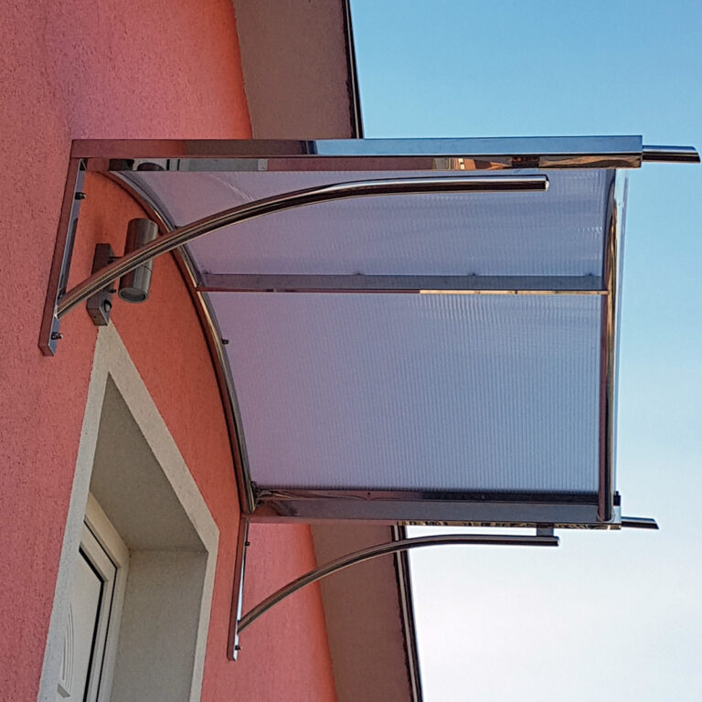 Moderna Nadstrešnica od inoxa sa zakrivljenim metalnim i prozirnim plastičnim dizajnom postavljena je iznad vrata na ružičastom štukaturnom zidu, nudeći hlad i zaštitu. Vedro plavo nebo pruža svijetlu pozadinu.